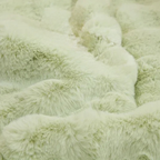 Zoom sur la fausse fourrure verte pastel, mettant en évidence la profondeur et la douceur du matériel, invitant à la détente dans un cadre serein.